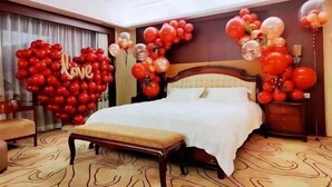 Une chambre d’hôtel avec un grand lit, une tête de lit en bois, un banc et un mur décoré de ballons rouges et blancs.