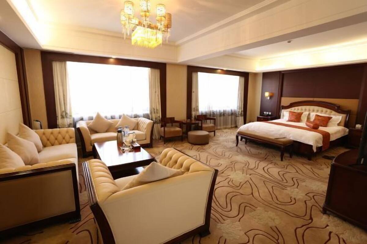 Une chambre d’hôtel avec un grand lit, deux canapés, une table basse et un lustre.
