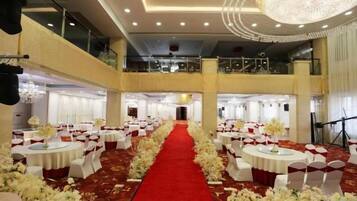 A banquet hall with round tables, a red carpet, and white floral arrangements.
