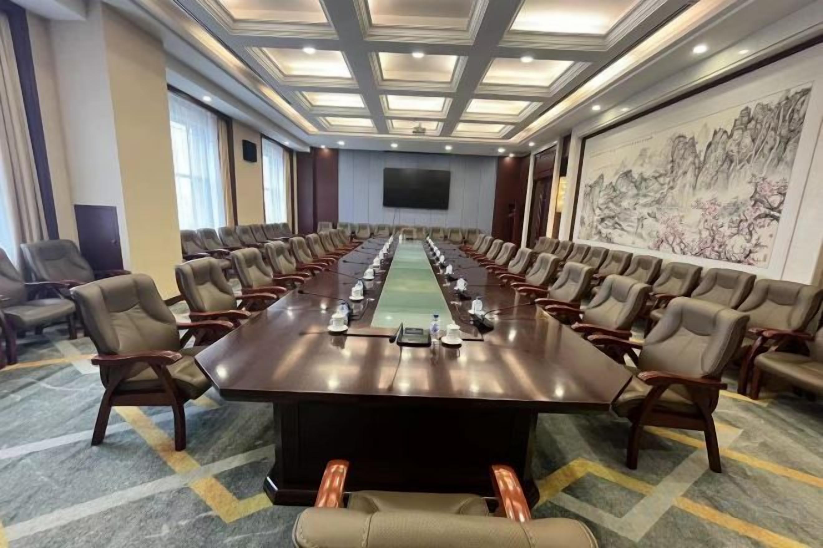 Una sala de conferencias con una larga mesa, varias sillas y una pantalla grande.