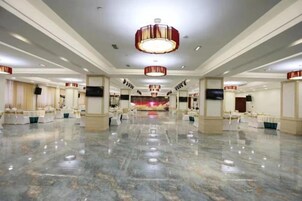 Un amplio vestíbulo de hotel con piso de mármol pulido, varias zonas de estar y un escenario central.