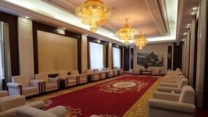 Une salle de conférence avec des rangées de chaises blanches, une moquette rouge et des lustres décoratifs.