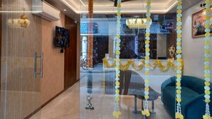 Un moderno vestíbulo de hotel con un separador de vidrio, un televisor, un sofá y guirnaldas florales decorativas.