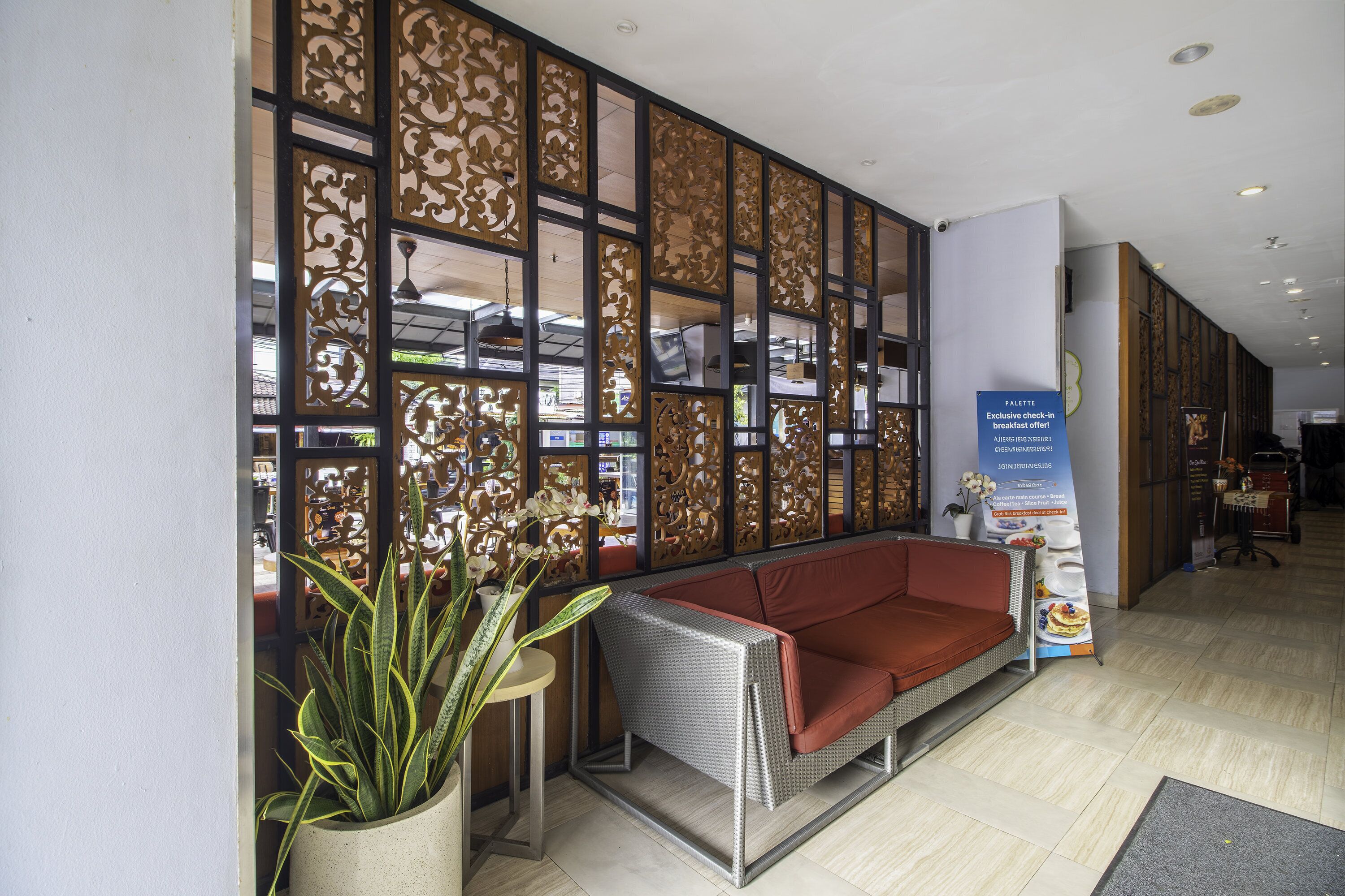 A reception area with a sofa, a potted plant, a decorative screen, and a signboard.