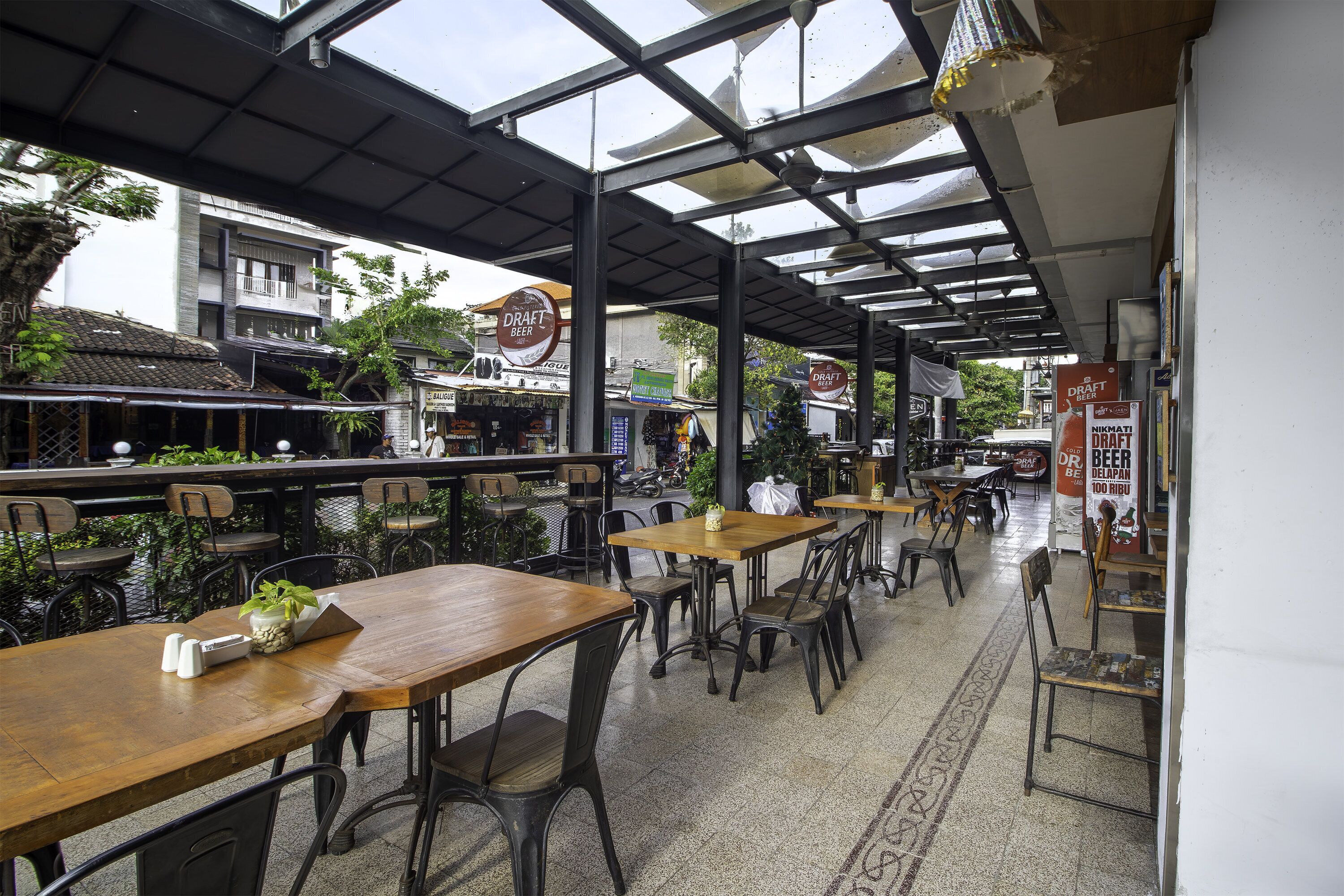 An outdoor café with wooden tables and chairs, a covered seating area, and signs for a draft beer and a restaurant.