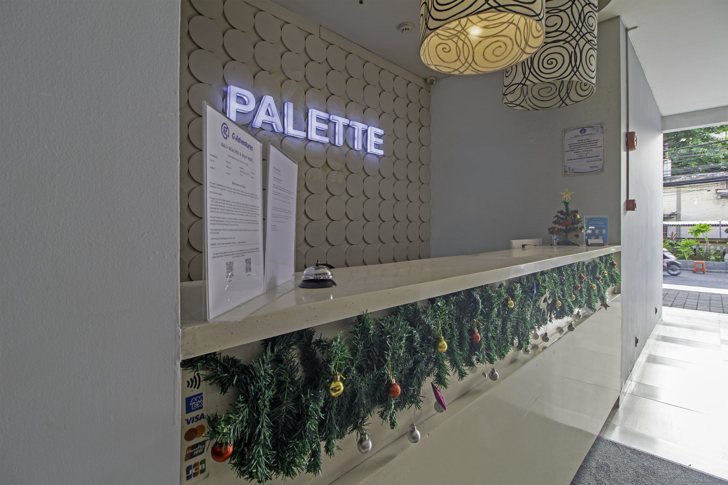 A reception desk with a neon sign reading 'PALETTE,' a decorative wall with circular patterns, and a Christmas garland with ornaments.