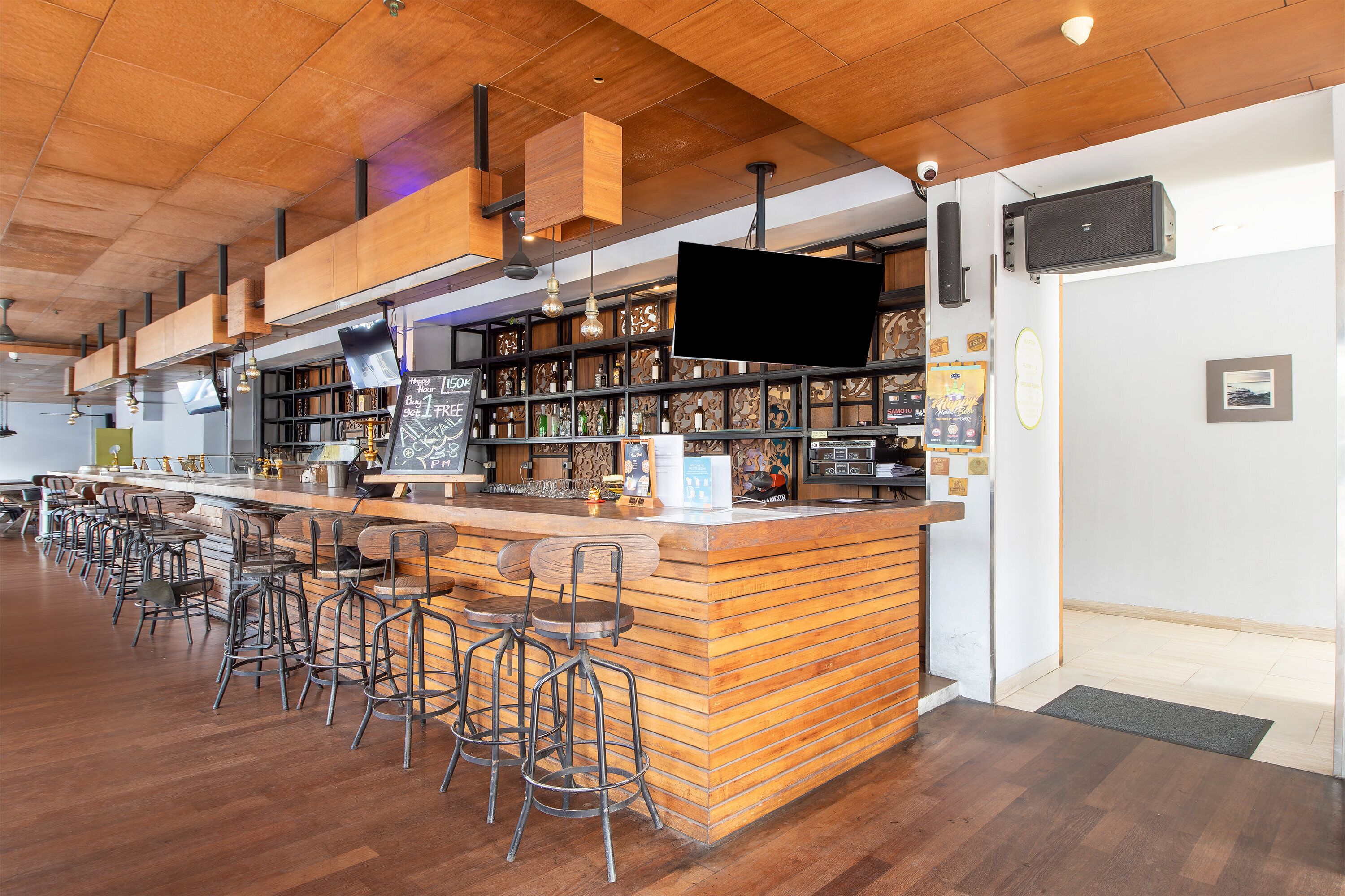 Un espace bar doté d’un comptoir en bois, de tabourets et d’étagères remplies de bouteilles.