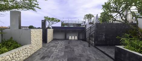 A rooftop patio with stone walls, a metal railing, and a view of a building in the background.