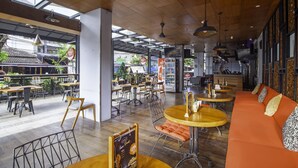 A modern cafe interior with wooden ceiling, round tables, orange seating, and a view of the street outside. - Palette Hotel near Padma (Legian)