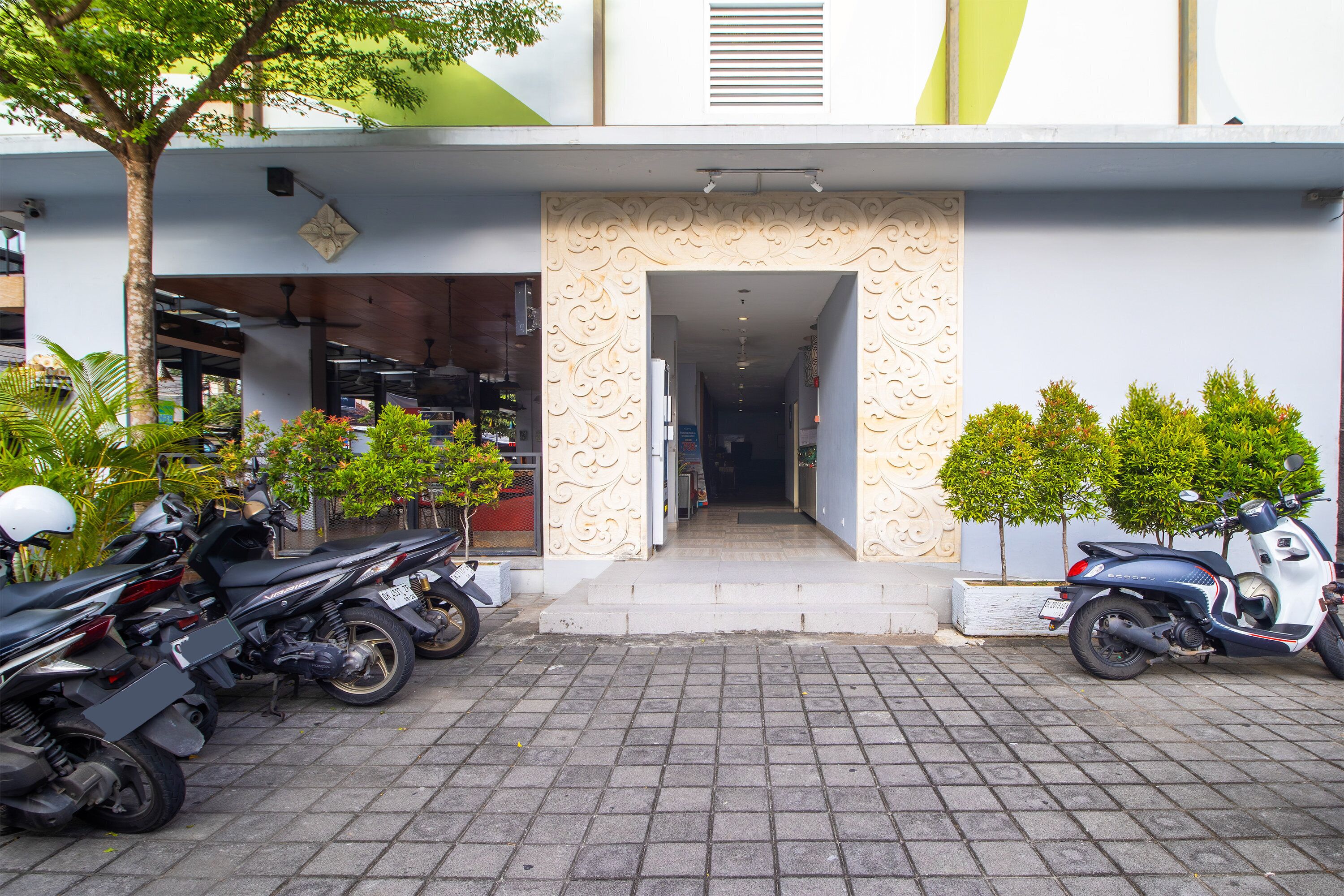 A building entrance with a paved driveway, a scooter, and several motorcycles parked outside.