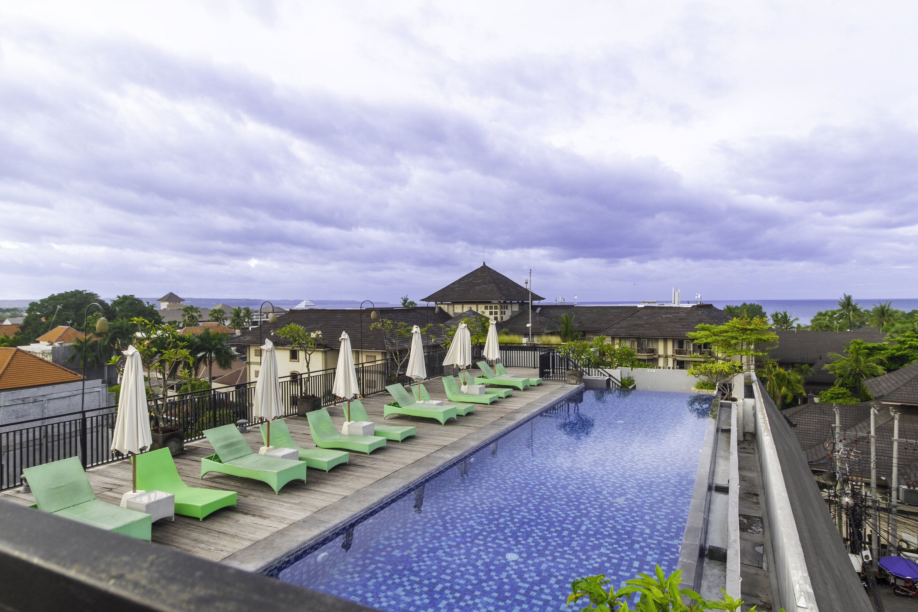 A swimming pool with lounge chairs and umbrellas, surrounded by buildings and a cloudy sky.