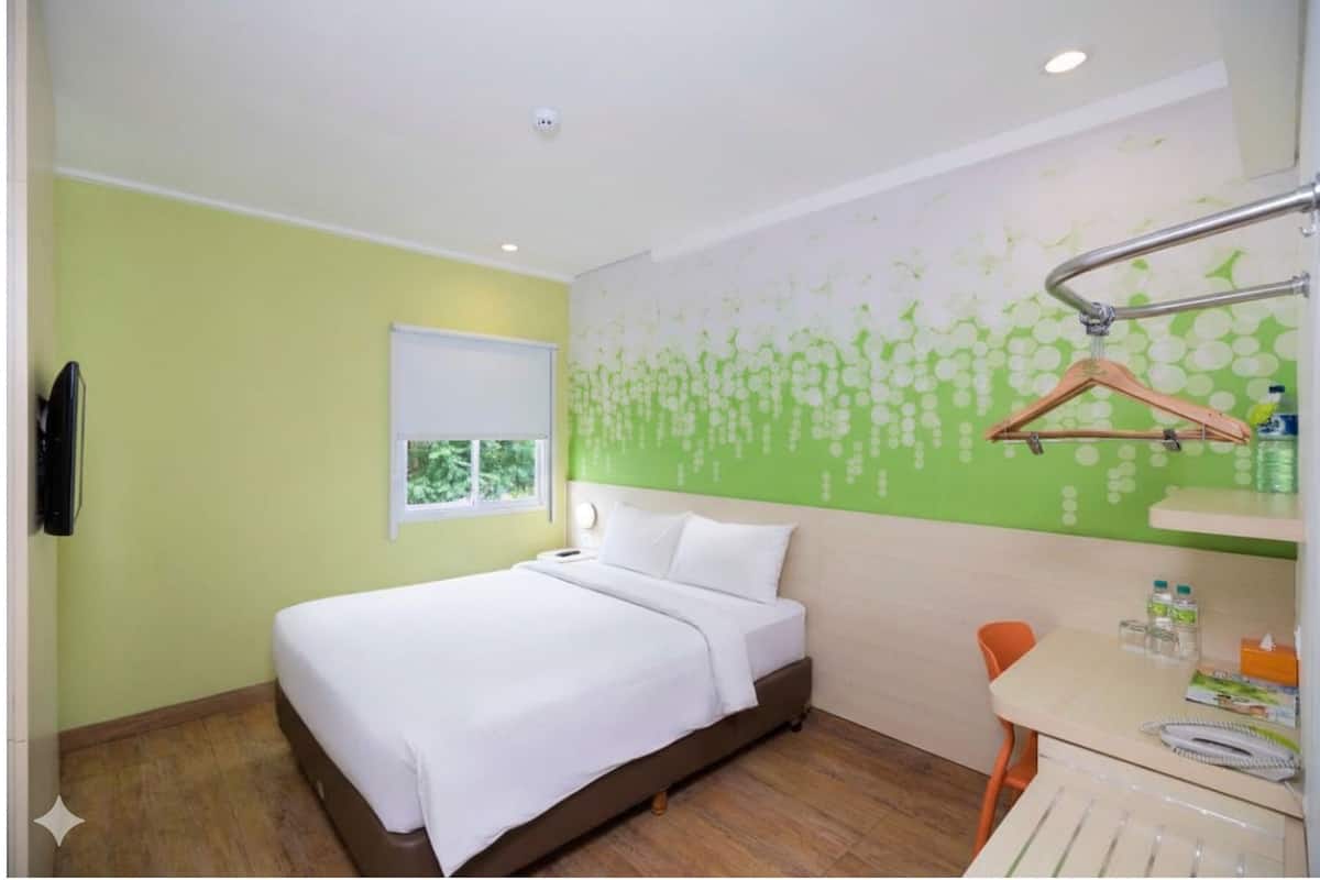 A hotel room with a bed, a desk with a chair, a window, and a wall-mounted TV.