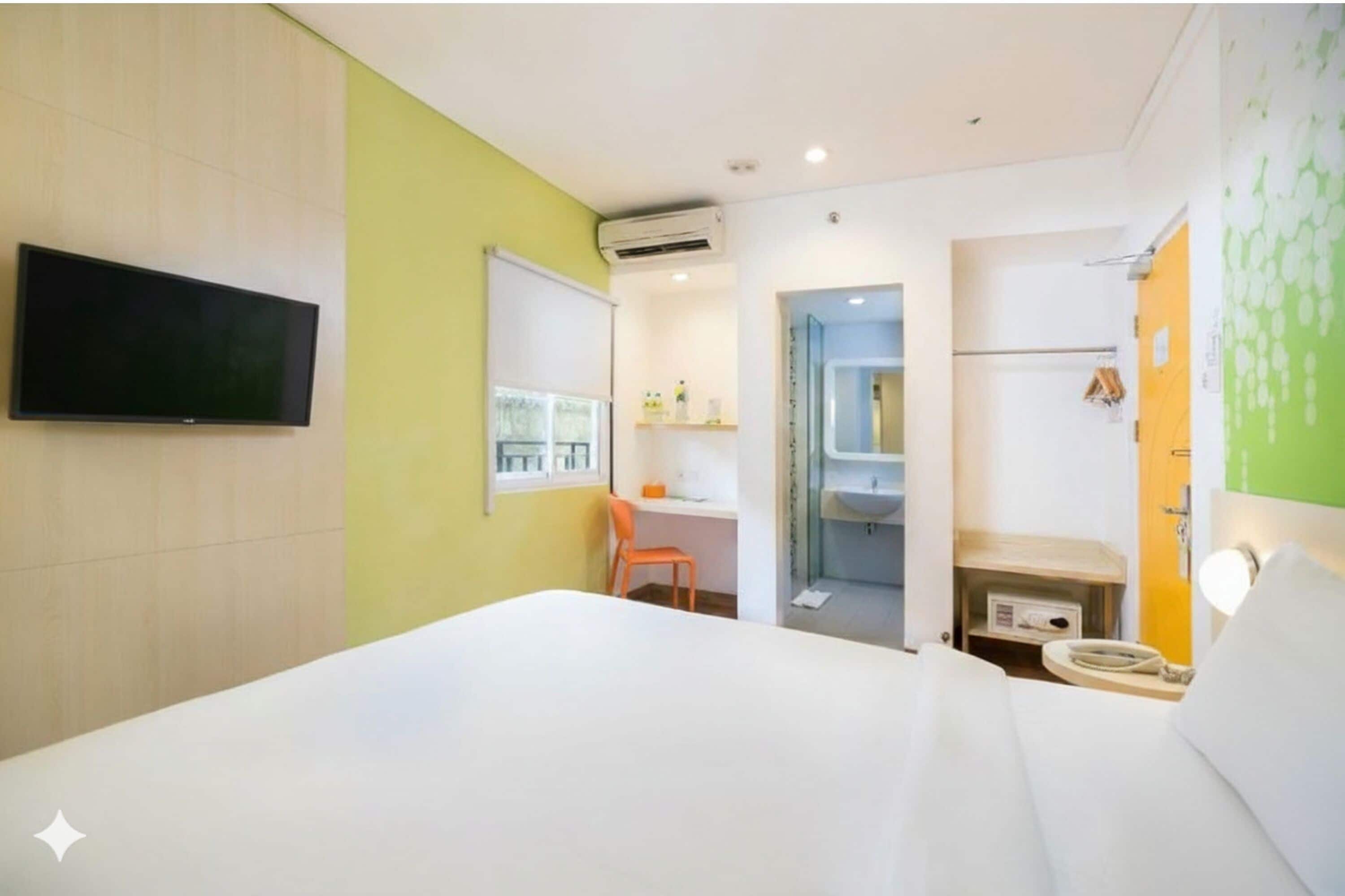 Habitación de hotel con cama, escritorio, silla, televisión y baño con lavabo y ducha.