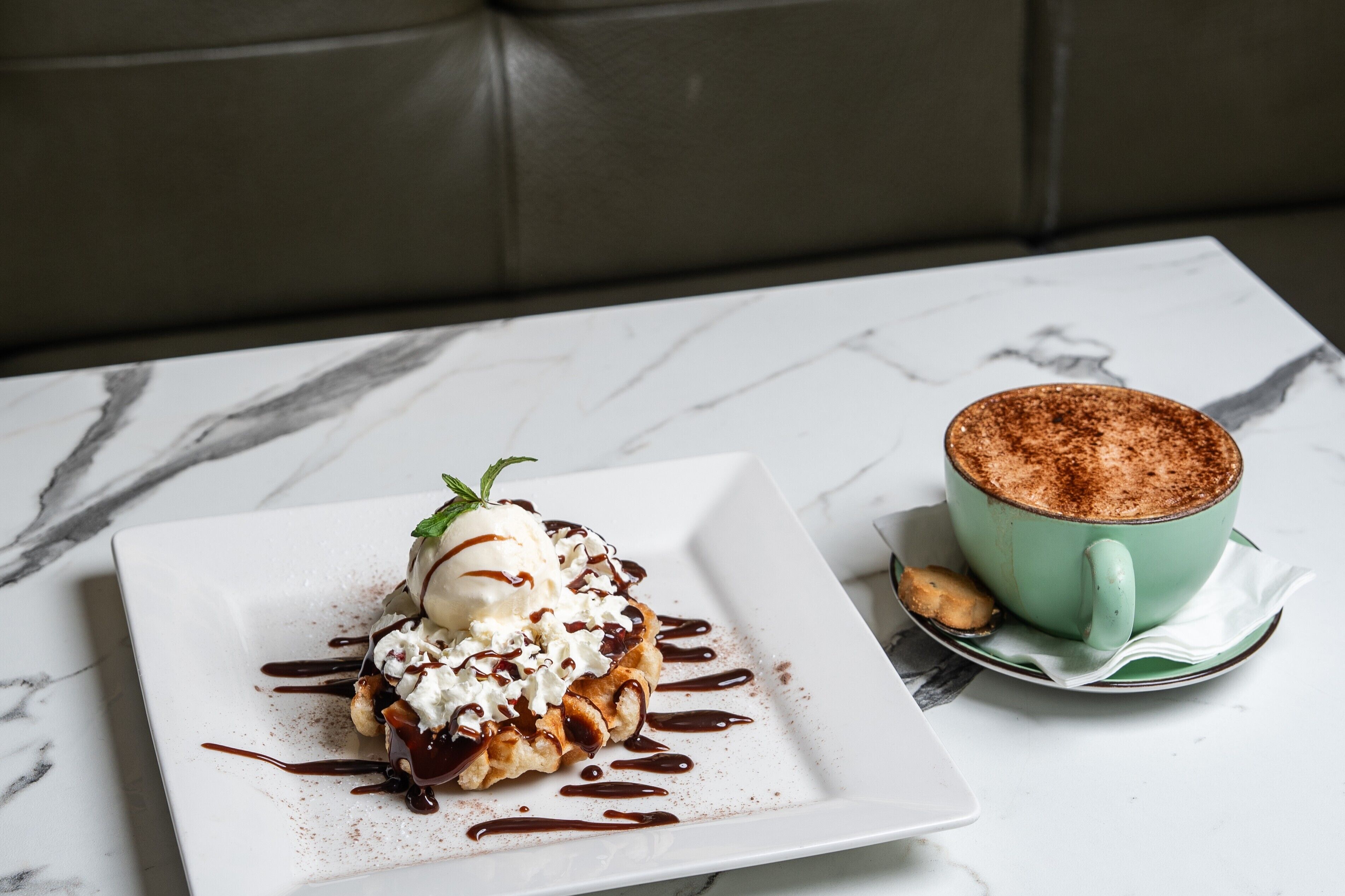 Un piattino con gelato e salsa al cioccolato, una tazza di caffè e un cucchiaio su un tavolo di marmo.