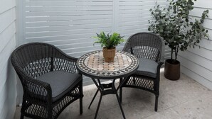 A patio with two wicker chairs, a round table with a woven center, and a potted plant.