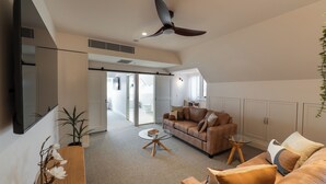 A modern living room with a ceiling fan, a brown sofa, a glass coffee table, and a potted plant.