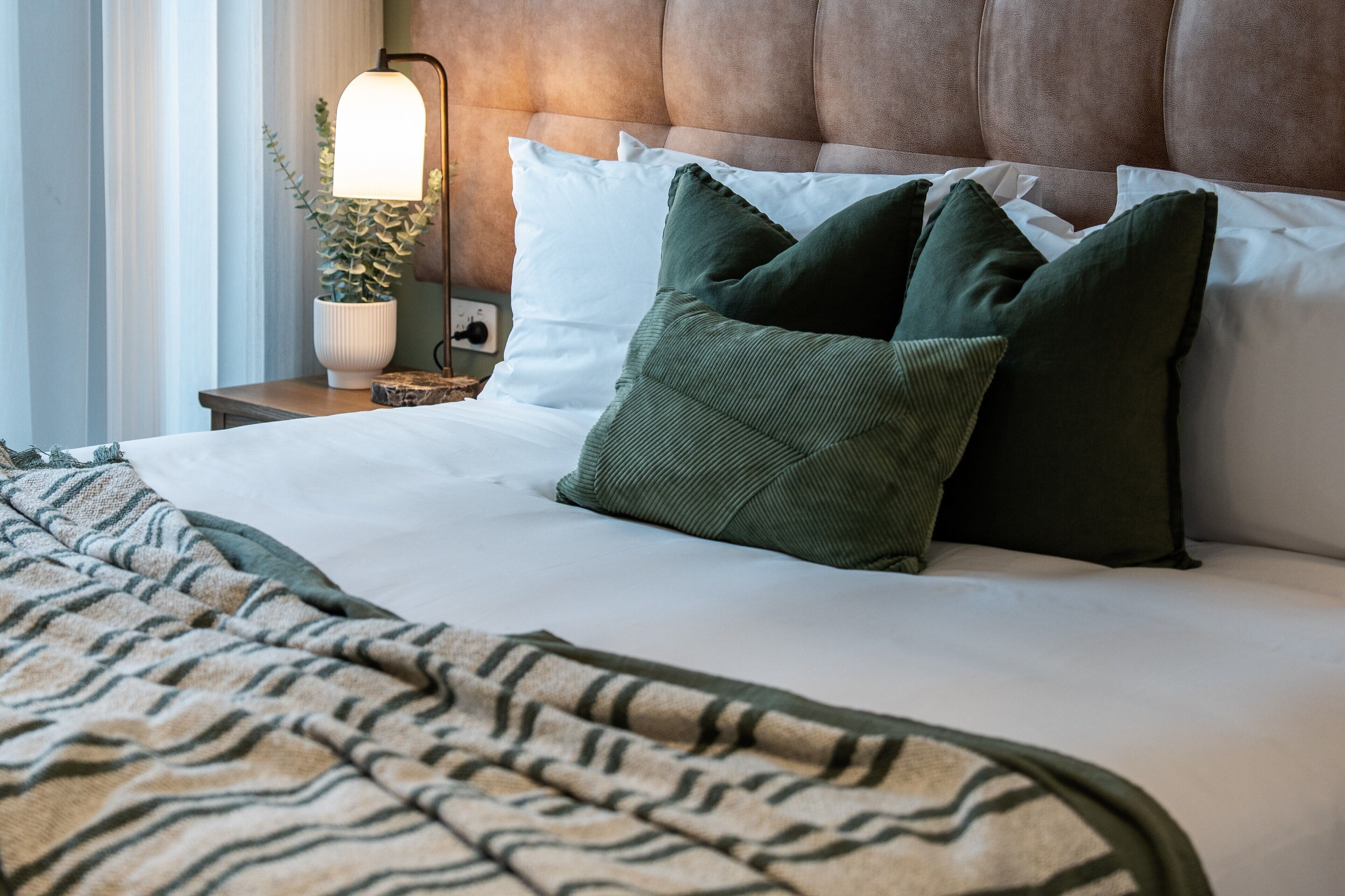 A neatly made bed with a striped blanket, a headboard, and a bedside lamp with a plant.