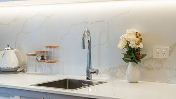 Uma cozinha com pia de aço inoxidável, backsplash de mármore branco e um vaso com flores sobre o balcão.