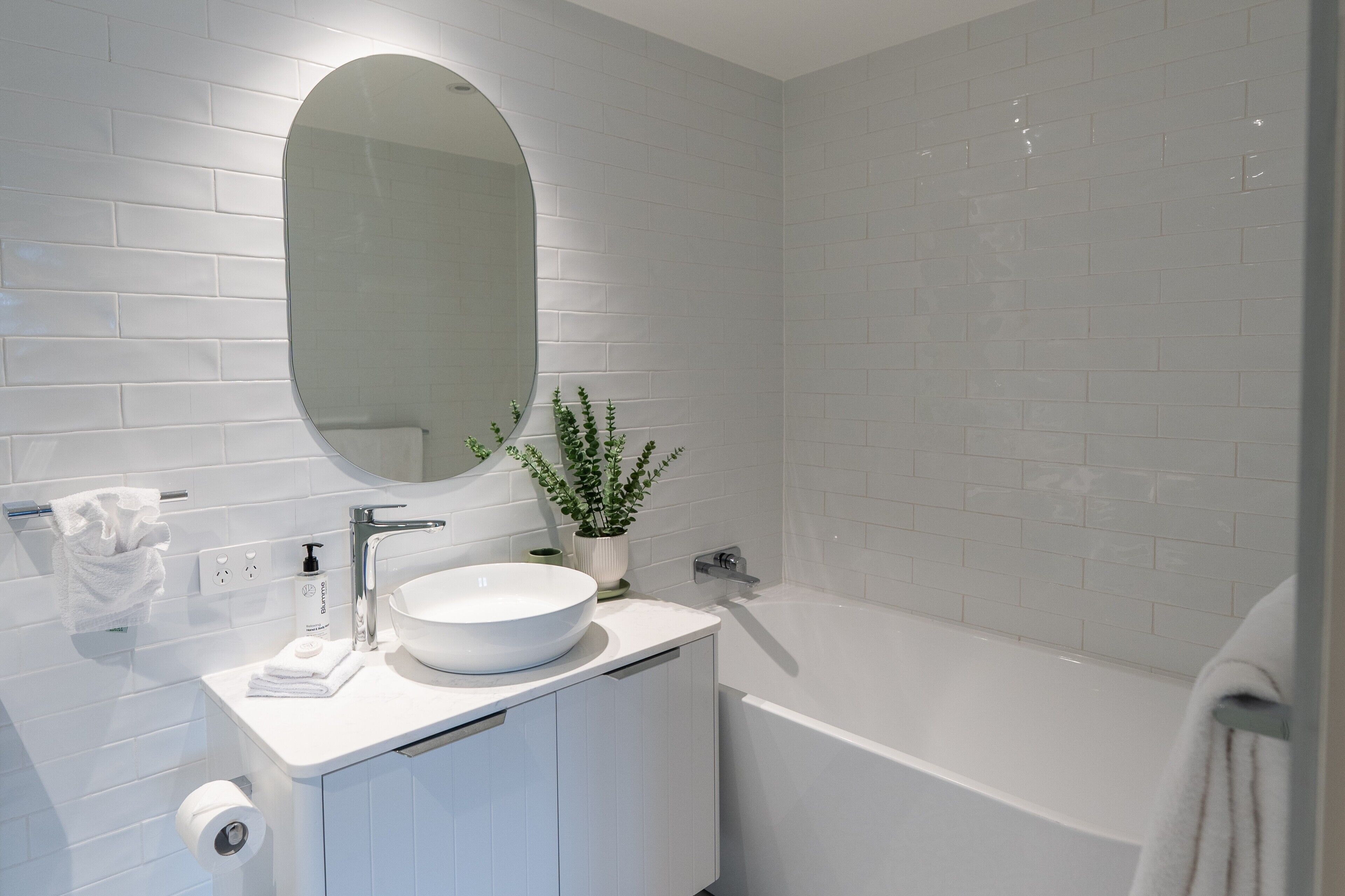 Een moderne badkamer met een wit wastafelmeubel, een ronde spiegel en een bad.