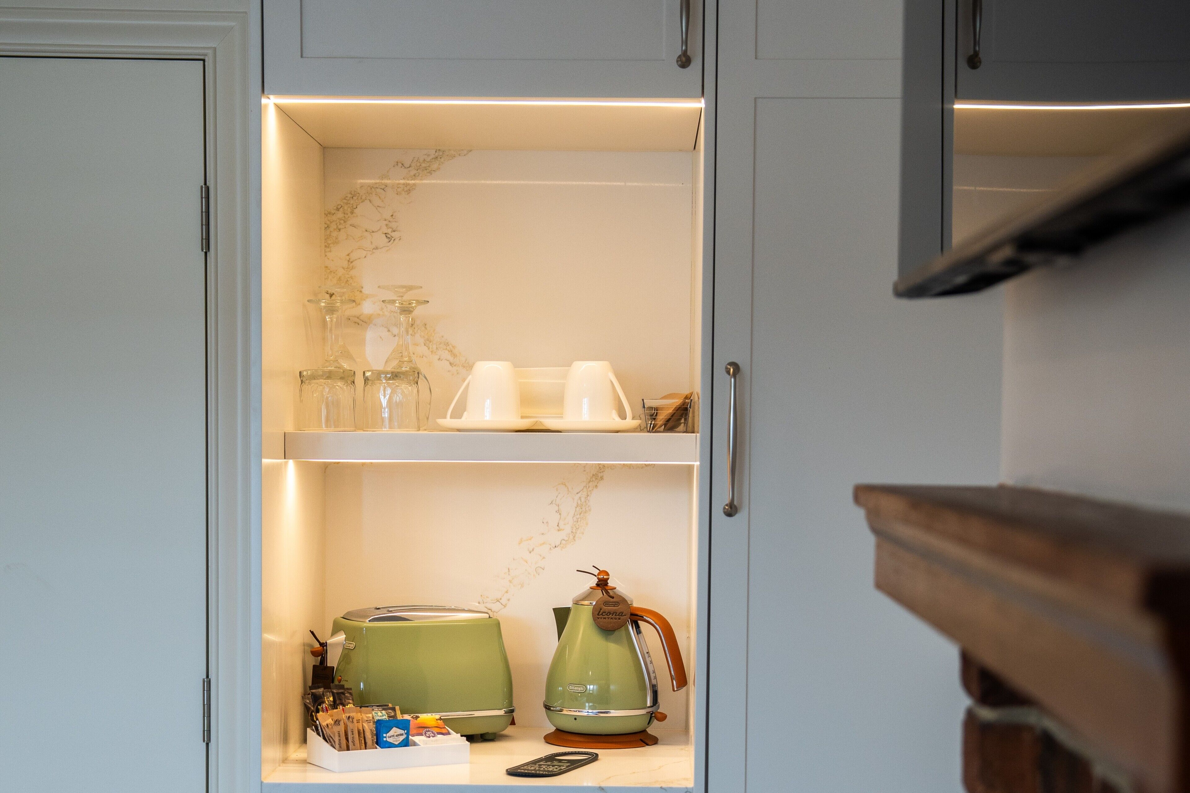 Una cocina con encimera de mármol, un hervidor verde, una cafetera y un control remoto.