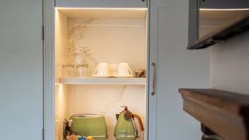 Una cocina con encimera de mármol, un hervidor verde, una cafetera y un control remoto.