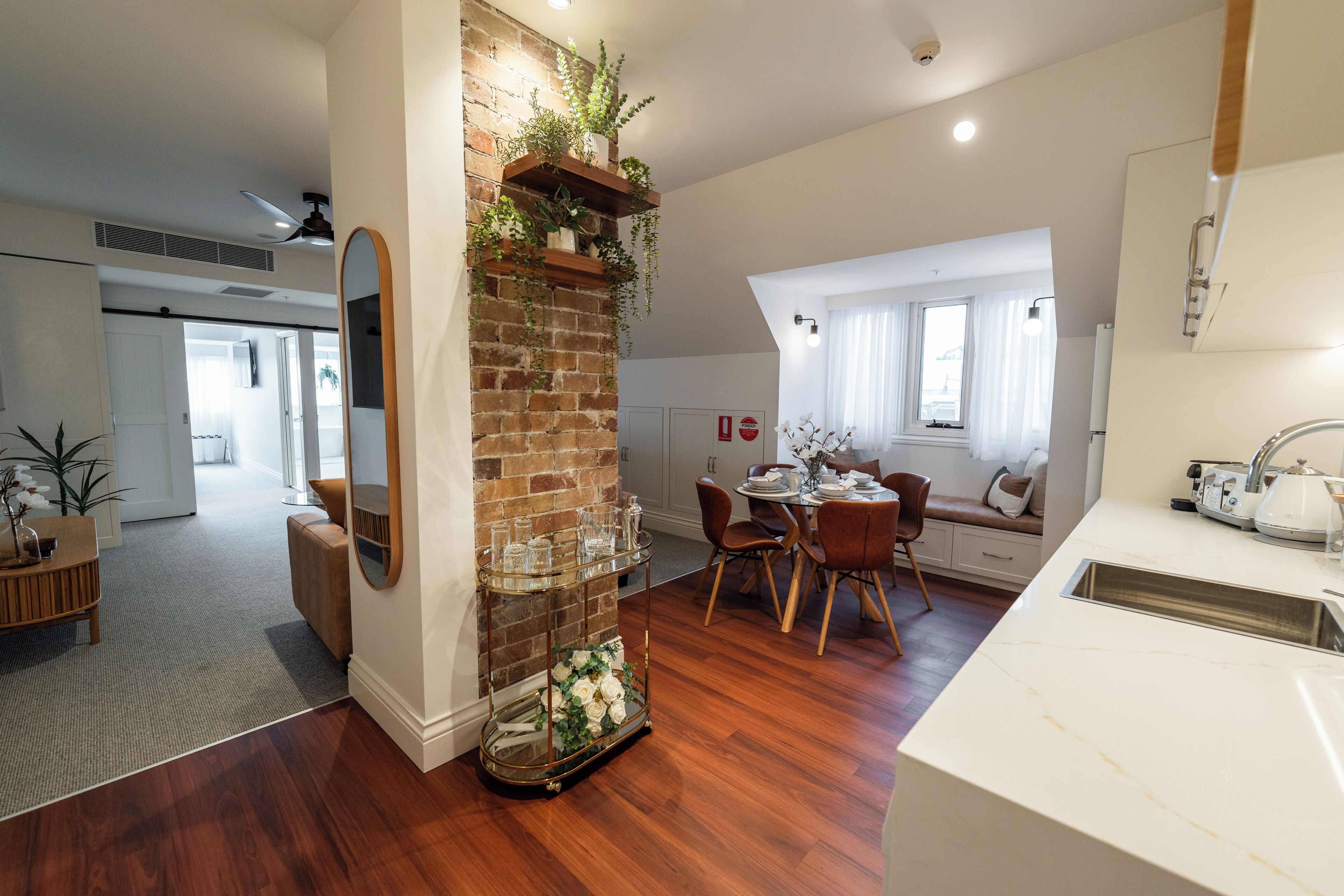 Una cocina moderna con pared de ladrillo, piso de madera y zona de comedor con mesa y sillas blancas.