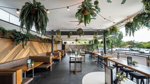 A restaurant with wooden booths, tables, hanging plants, and a view of the street. - Camden Hotel Suites (Camden)