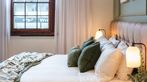 A neatly made bed with a striped blanket, green and white pillows, and a bedside lamp.