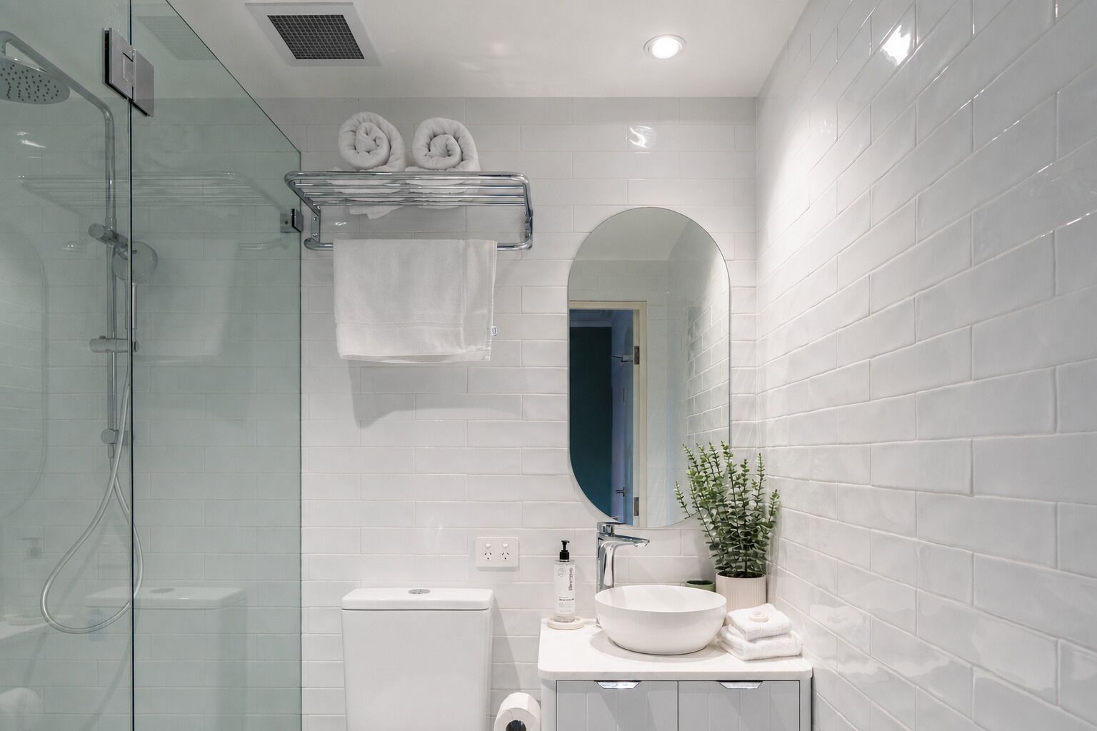 A modern bathroom with a glass shower enclosure, a white toilet, a sink with a bowl, and a mirror.