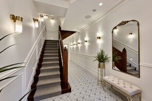 A grand staircase with a patterned carpet, wall-mounted lights, and a large mirror. - Camden Hotel Suites (Camden)