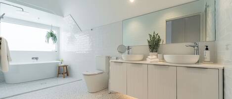 A modern bathroom with a freestanding bathtub, a large mirror, and a double sink vanity.