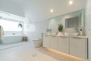 A modern bathroom with a freestanding bathtub, a large mirror, and a double sink vanity. - Camden Hotel Suites (Camden)