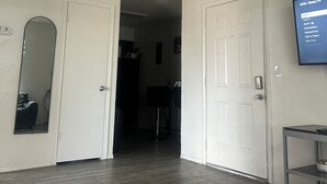 Um corredor com uma porta que dá para outro quarto, uma TV montada exibindo um menu, e um espelho na parede esquerda.
