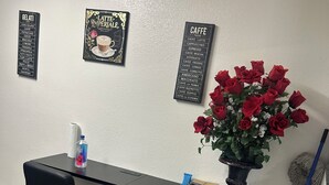 Uma área de bar com dois banquetas pretas, um balcão de bar preto, um arranjo de rosas vermelhas em vaso, e placas pretas fixadas na parede listando bebidas.