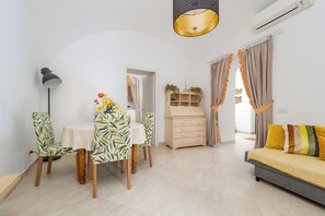 A modern living room with a dining area, a sofa, a lamp, and a ceiling light fixture. - Citrus Garden House (Piano di Sorrento)