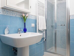 A bathroom with a white sink, blue tiles, a glass shower enclosure, and a white towel rack. - Citrus Garden House (Piano di Sorrento)