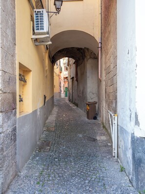 A narrow cobblestone alleyway with a stone archway, flanked by buildings with visible pipes and a trash bin. - Citrus Garden House (Piano di Sorrento)