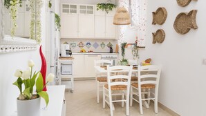 A modern kitchen with white cabinets, a dining area with white chairs, and a small table. - Citrus Garden House (Piano di Sorrento)