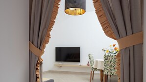 A modern living room with a flat-screen TV, a small table, and a bench. - Citrus Garden House (Piano di Sorrento)