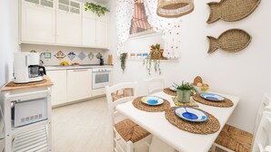 A kitchen with white cabinets, a coffee machine, and a dining table set with plates and a vase. - Citrus Garden House (Piano di Sorrento)