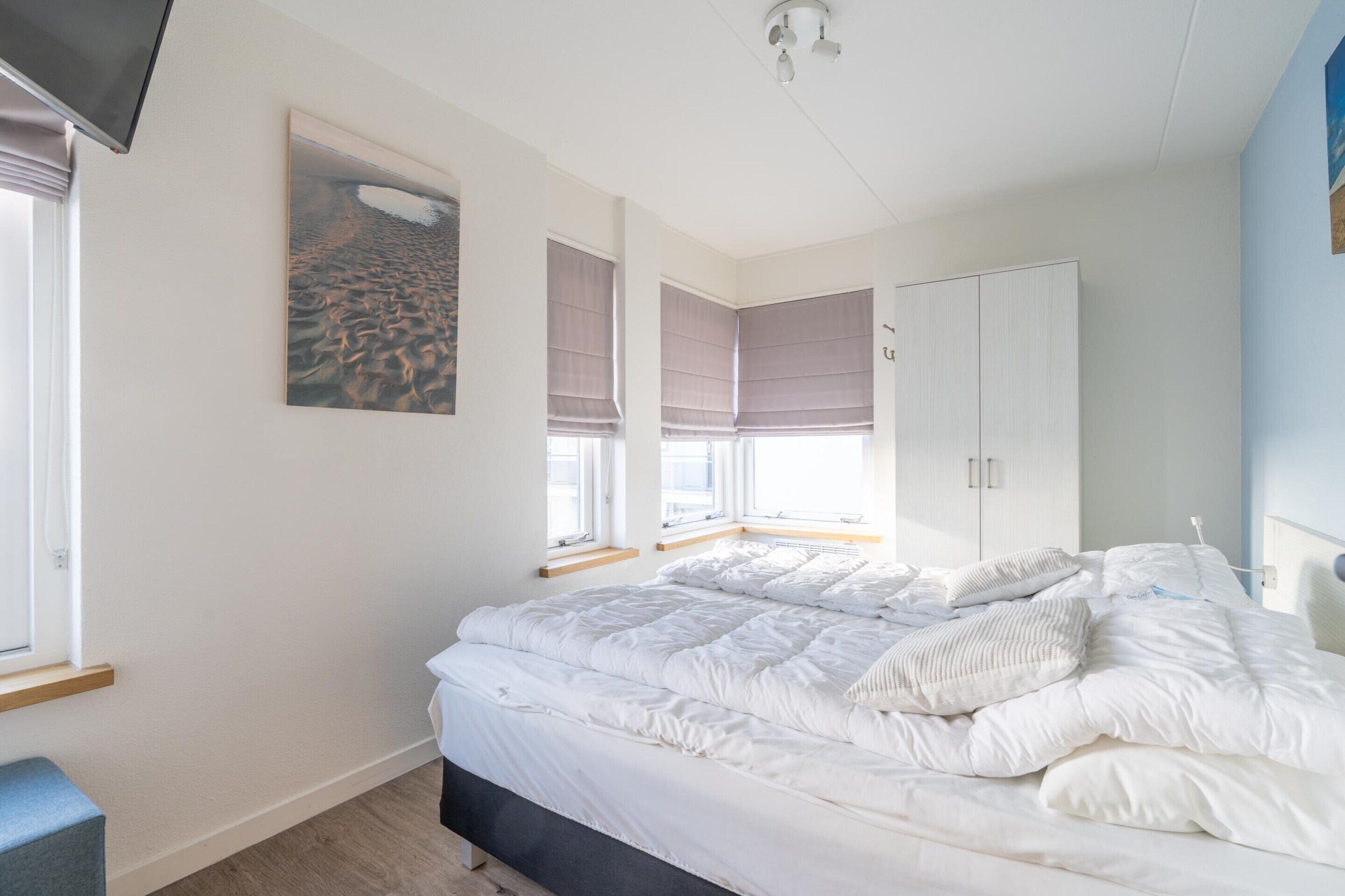 A bedroom with a bed, a wardrobe, a window, and a painting on the wall.
