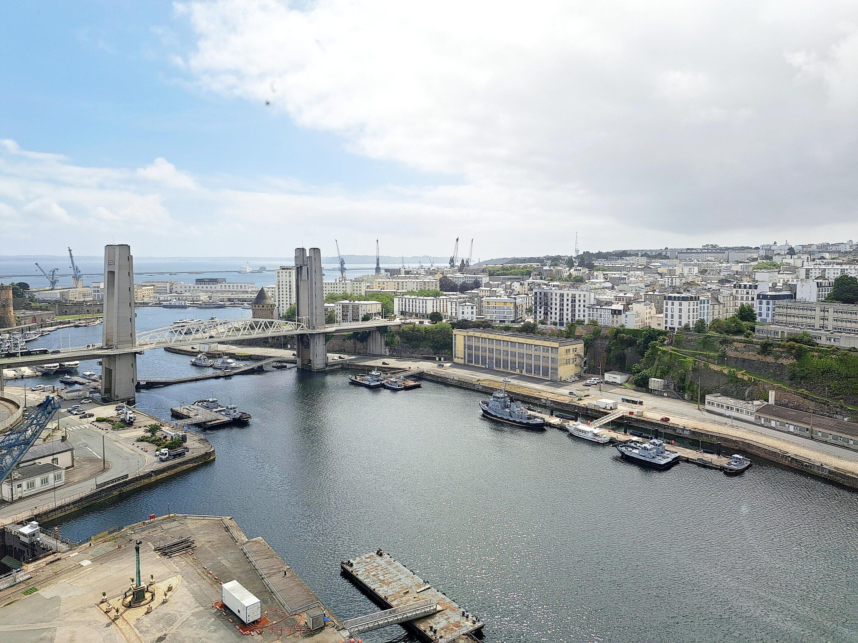 A harbor with a bridge, boats, and industrial buildings.