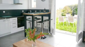 A modern kitchen with a dining area, a clock on the wall, and a view of the garden through the glass door. - Apartment in Lilia Near Kastell Ac"h Strand (Plouguerneau)