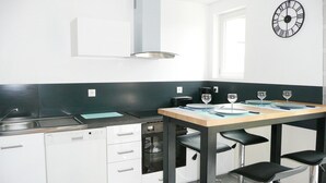 A modern kitchen with white cabinets, a stainless steel sink, a black countertop, and a wooden table set for dining. - Apartment in Lilia Near Kastell Ac"h Strand (Plouguerneau)