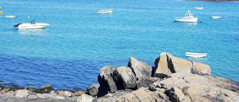 A rocky shoreline with several boats, including a blue rowboat and a white motorboat, near calm blue waters.