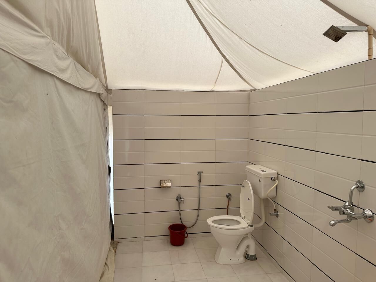 Une petite salle de bain fermée, avec des murs recouverts de carreaux blancs, des toilettes blanches et une douche.