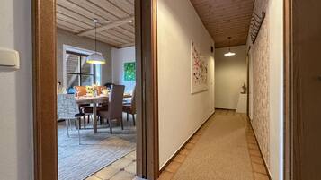 A hallway with a wooden ceiling, a dining area with a table and chairs, and a patterned floor.