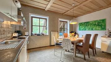 A kitchen with wooden ceiling beams, a dining area with a table and chairs, and a green wall art piece.