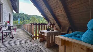 A wooden deck with a table and chairs, a cushioned bench, and a potted plant.