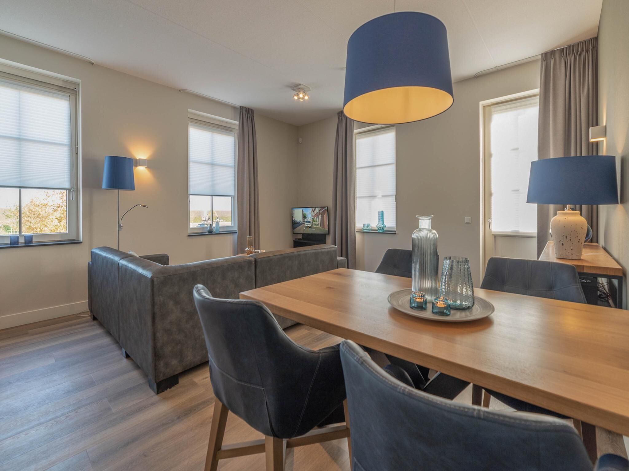 A modern living room with a wooden dining table, grey sofa, and a large blue pendant light.